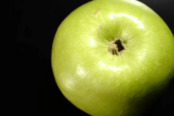 A green apple on a black background. Closeup. The light was dim.