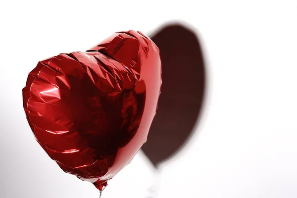 Een hart opgeblazen met helium vliegt op een touwtje op een witte achtergrond. Een geschenk voor Valentijnsdag. — Stockfoto