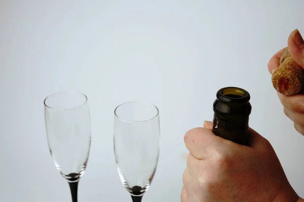 Otwieramy butelkę szampana na białym tle w okularach. Dłonie i korek są widoczne. — Zdjęcie stockowe