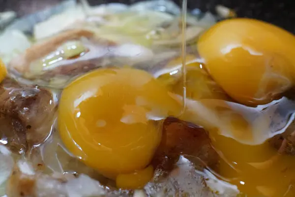 鸡蛋的蛋黄被碎在正在煎锅里烹调的猪肉和洋葱上. — 图库照片