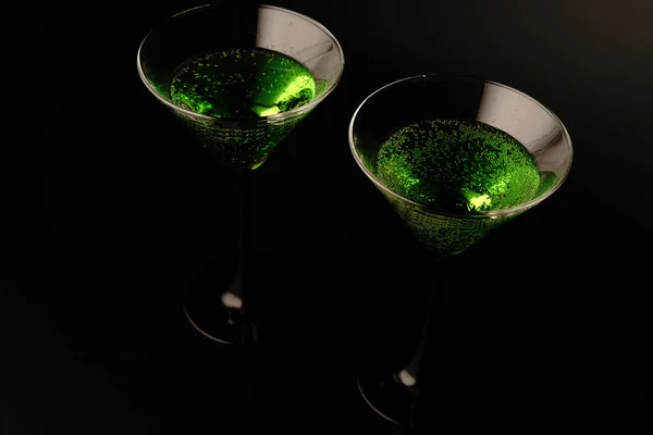 黒を基調としたグリーンのカクテル2杯。一方のガラスは満杯でもう一方は空です — ストック写真