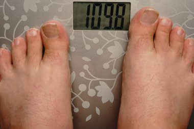 İki erkek bacağı terazide duruyor. Ağırlığı neredeyse yüz on kilogramdan fazla..