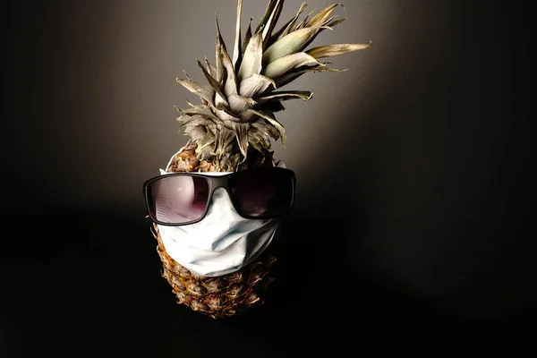Ananas bär solglasögon och en medicinsk mask på en svart bakgrund. Plats för text — Stockfoto