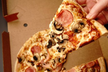 Mantarlı bir dilim pizza ve jambon elle alınır. Üst Manzara. Stüdyo çekimi