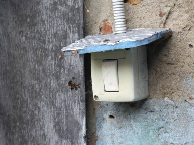 Köyün caddesine plastik beyaz ışık anahtarı monte edilmiş. Yağmura dayanıklı bir çatısı var. Duvara iliştirilmiş