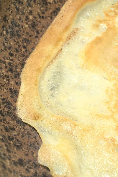 Une fine crêpe dorée est frite dans une poêle. Gros plan. Instantané vertical — Photo