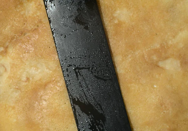 Une fine crêpe de couleur dorée sur elle se trouve une spatule chefs de couleur noire. Vue du dessus — Photo