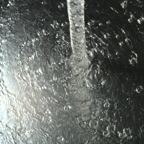 金属色の表面に水のジェットが落ちる。光と水の遊びが見える。垂直スナップショット — ストック写真