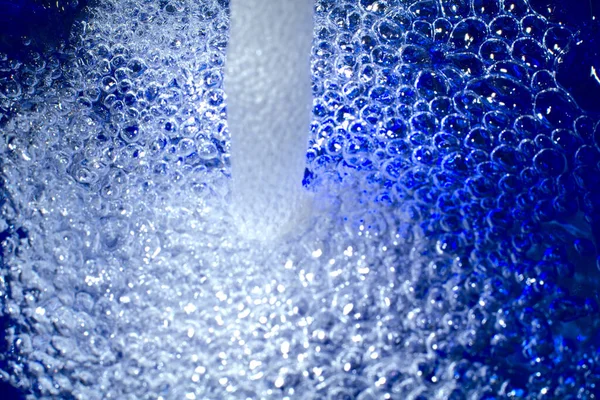 El agua se vierte en un plato azul. Burbujas y un patrón de color interesante son visibles. Primer plano. —  Fotos de Stock