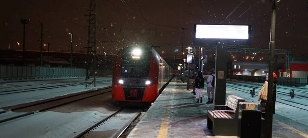 Moscou, Russie-16 février 2021 : Un train entrant de Moscou de diamètre central et son projecteur lumineux illuminent la gare. Sa nuit et sa neige. Instantané vertical — Photo