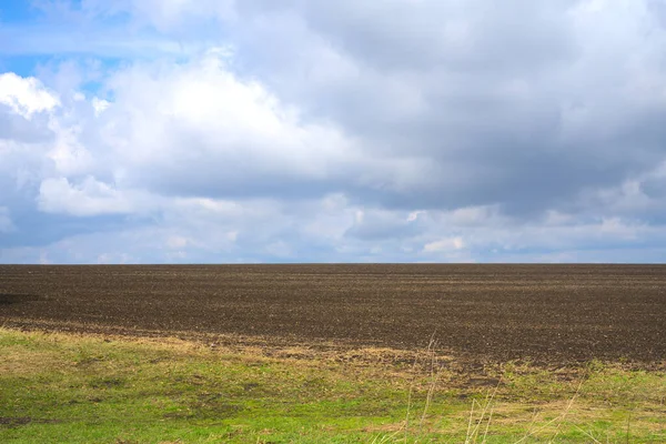 Gräs och plöjningsfält. Blå himmel och vita moln. Våren — Stockfoto