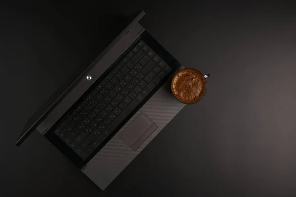 Laptop y una taza de café negro sobre un fondo plano negro. Luces atenuadas. —  Fotos de Stock