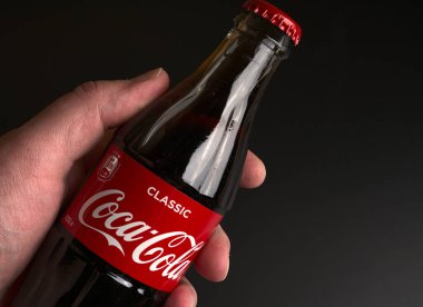 Moskova, Rusya - 20 Mayıs 2021: Siyah arka planda bir eli olan cam Coca Cola şişesi. Yaklaştın. Sönük ışıklar