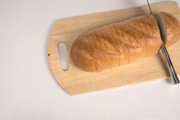 Il pane affettato giace su un tagliere con un coltello su fondo bianco. Spazio per il testo. Vista dall'alto — Foto Stock