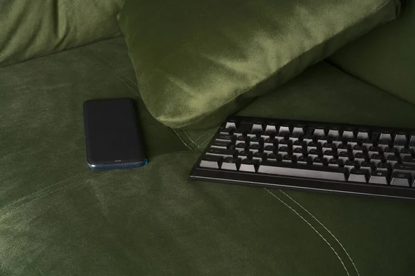 O teclado e o telefone celular estão deitados no sofá macio. — Fotografia de Stock