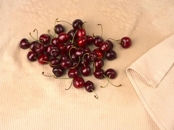 A lot of cherries lie on a light brown towel. — Stock Photo, Image