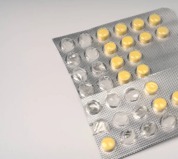 Yellow small tablets in a large package on a white background closeup. — Stock Photo, Image