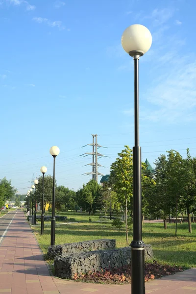 Letni park na obrzeżach dużego miasta ze ścieżkami rowerowymi i ozdobionymi słupami oświetleniowymi. — Zdjęcie stockowe