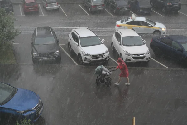 Moscow, Russia - june 28 2021: There is a downpour in the city and there are parked cars on the road. A woman with a stroller under an umbrella tries to escape from the rain Fotos de stock libres de derechos