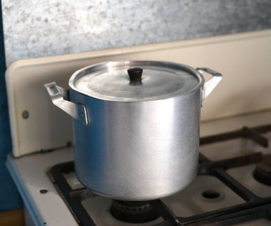 Eski bir alüminyum tencere eski bir gaz sobasının üzerinde duruyor.