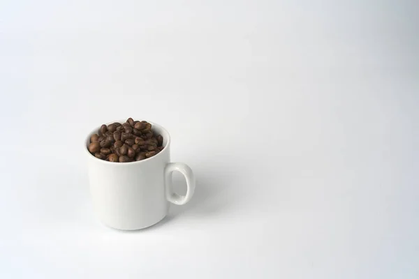 Chicchi di caffè si trovano in una tazza di caffè bianco su uno sfondo bianco. — Foto Stock