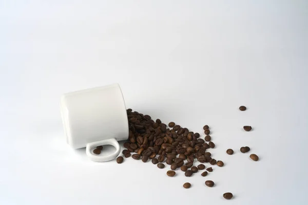 Una tazza di caffè bianco è caduto e chicchi di caffè fuoriuscito su uno sfondo bianco. — Foto Stock