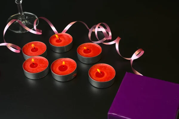 Burning small red candles and a champagne glass with a pink ribbon on a black background. — Stock Photo, Image