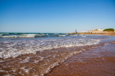 Sahilde, arkasında dağlar olan bir dalganın görüntüsü. Reklam panosu kuran adamlar. Ras Al Khaimah Emirlik 'te çekilmiş. BAE. Açık havada.