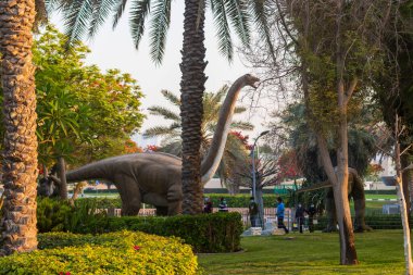 Dubai, BAE - 05.11.2021 Dinozor parkındaki austrosaurus kopyalarını inceleyen ziyaretçiler.