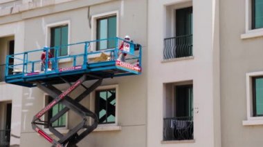 Yükseklerde çalışan bakım işçileri, Uluslararası şehir bölgesindeki binanın ön cephesini onarıyorlar. Açık havada.