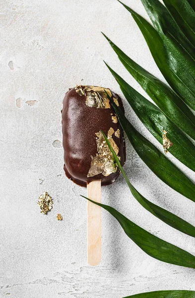 Popsicles, covered with chocolate, with a leaf of edible gold on top on a light concrete background. Popsicle and sweet dessert on a stick. Selective focus