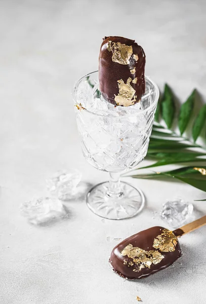 Popsicles, covered with chocolate, with a leaf of edible gold on top on a light concrete background. Popsicle and sweet dessert on a stick. Selective focus