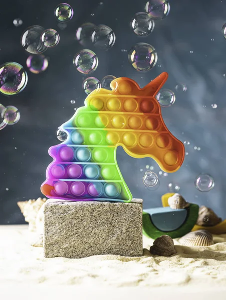 Pop it toy, rainbow colors, in the form of a unicorn on the podium on a bright background. Multi-colored, sensory anti-stress toy fidget pop it and soap bubbles. Selective focus