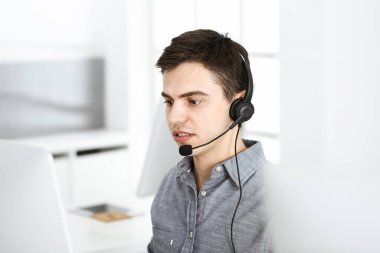 İnternette müşterilerle konuşurken kulaklık ve bilgisayar kullanan sıradan giyinmiş genç bir adam. Çağrı merkezi, iş konsepti