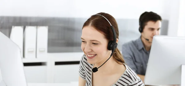 Casual dressed young woman using headset and computer while talking with customers online. Group of operators at work. Call center, business concept — Stock Photo, Image