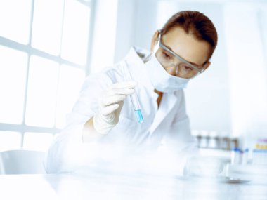 Kadın laboratuvar asistanı mavi sıvıyla test tüpünü analiz ediyor. Tıp, sağlık ve araştırma konsepti