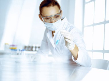 Kadın laboratuvar asistanı mavi sıvıyla test tüpünü analiz ediyor. Tıp, sağlık ve araştırma konsepti