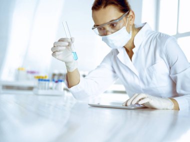 Kadın laboratuvar asistanı mavi sıvıyla test tüpünü analiz ediyor. Tıp, sağlık ve araştırma konsepti