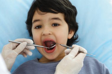 Tatlı Arap çocuk doktorla sözlü kontrol sırasında ağzı açık bir şekilde dişçi koltuğunda oturuyor. Dişçi muayenehanesi. Stomatoloji kavramı