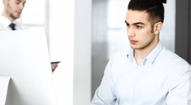 İşadamı modern ofiste bilgisayarla çalışıyor. Arap erkek girişimcinin iş yerindeki portresi. İş konsepti