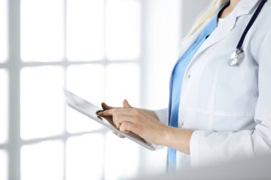 Bilinmeyen kadın doktor klinikte duruyor ve tablet bilgisayar kullanıyor, yakın plan. Tıp ve sağlık alanlarındaki veriler