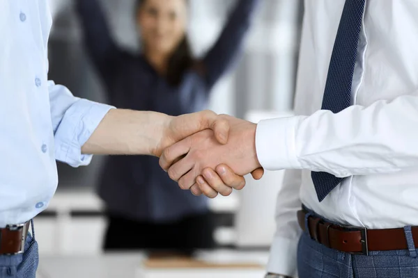 2人のビジネスマンのオフィスで、クローズアップ握手している。背景には手を挙げて幸せと興奮のビジネスウーマンが立っています。ビジネス界の概念 — ストック写真