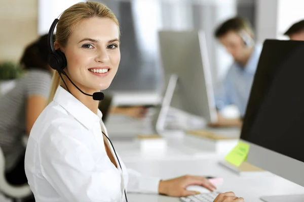 顧客サービスオフィスでのコミュニケーションやコンサルティングにヘッドセットを使用してブロンドのビジネス女性。コールセンター。業務を行う者の集団 — ストック写真