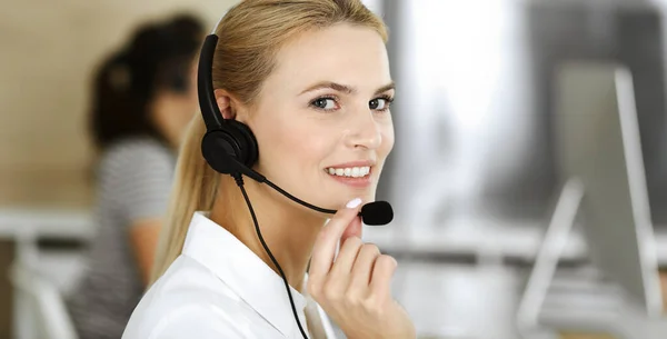金发女商人使用耳机与客户服务办公室的人进行交流和咨询。呼叫中心工作中的操作者群体 — 图库照片