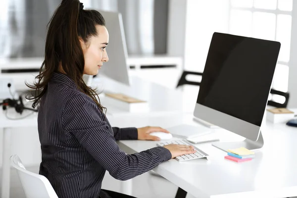 Mujer de negocios que utiliza la computadora en el lugar de trabajo en la oficina moderna. Secretaria morena o abogada sonriendo y se ve feliz. Trabajar por placer y éxito —  Fotos de Stock