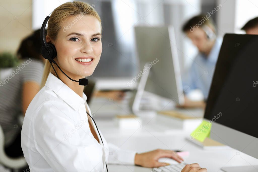 Blonde business woman using headset for communication and consulting people at customer service office. Call center. Group of operators at work