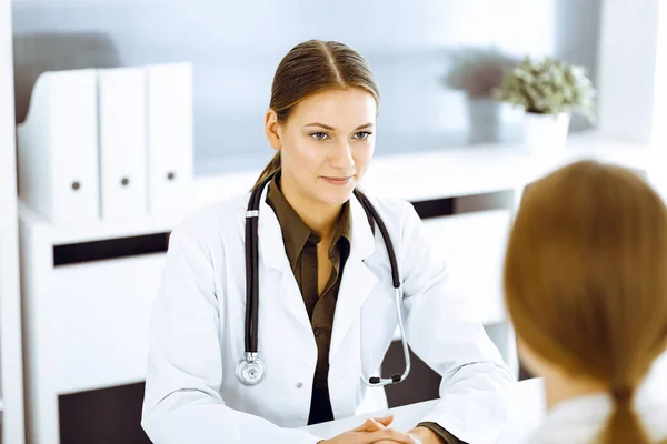 Mujer-médico y paciente sentados y hablando en el consultorio del hospital. Blusa de color verde se adapta al terapeuta — Foto de Stock