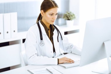 Hastane ofisindeki masada otururken bilgisayar başında daktilo yazan kadın doktor. Doktor iş başında.