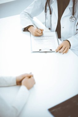 Bilinmeyen kadın-doktor ve kadın hasta klinikteki tıbbi muayenede oturuyor ve konuşuyor, yakın plan. Yeşil bluz giyen terapist ilaç geçmişini dolduruyor. Tıp konsepti