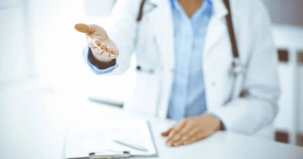 Donna-medico sconosciuta in camicetta blu sta dando la mano mentre si siede alla scrivania in clinica. Servizio medico perfetto, concetto di medicina — Foto Stock